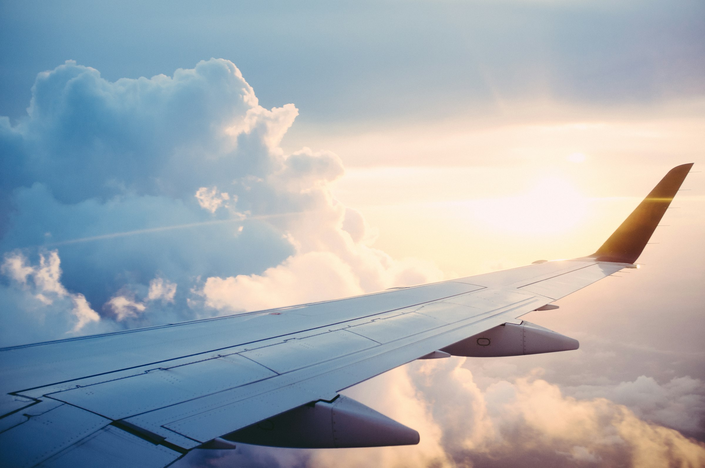 View over a private jet's wing above the clouds at golden hour